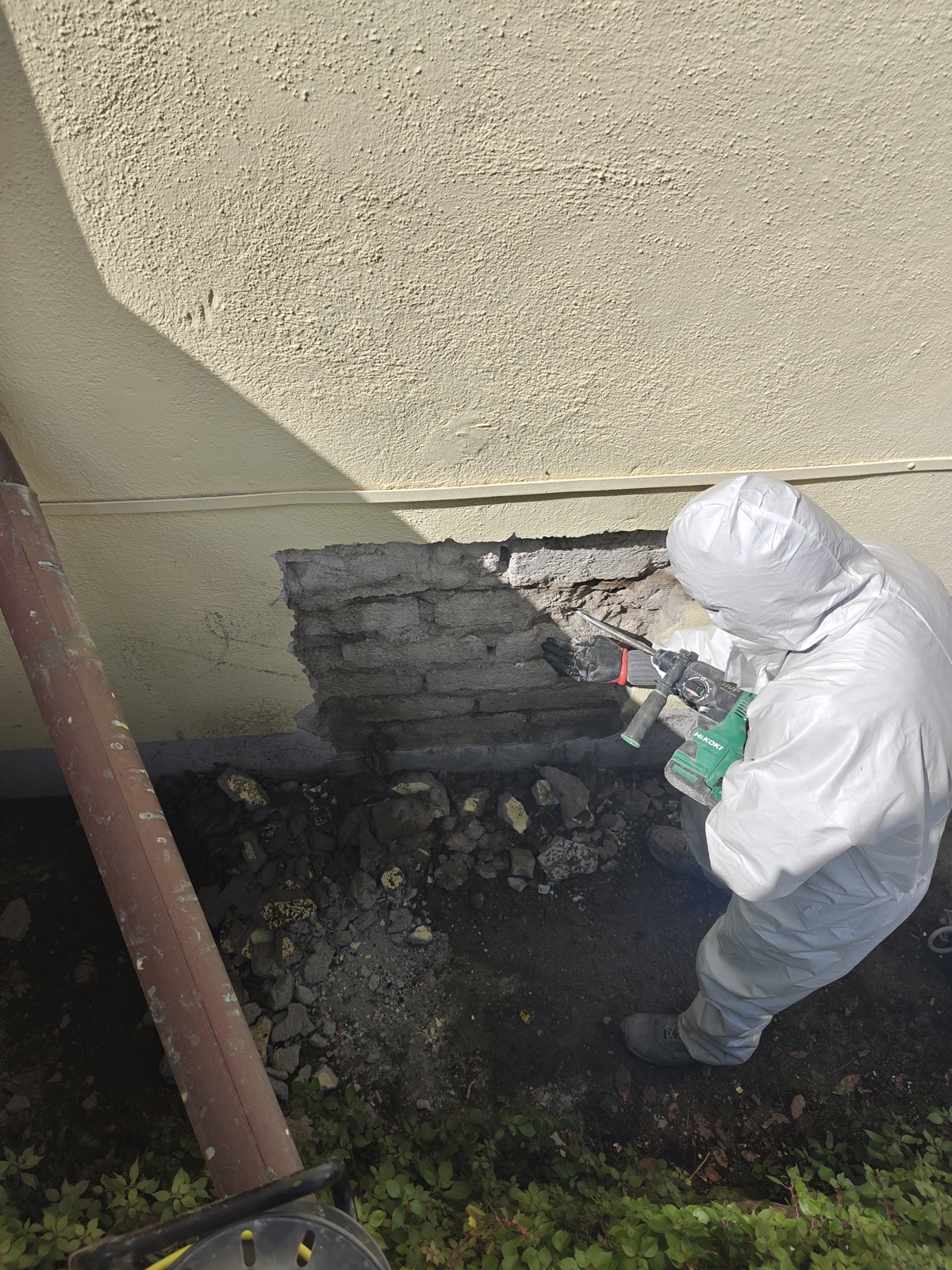 Operatore IPCS in tuta DPI integrale durante prelievo di campione di malta da muratura esistente di edificio scolastico in Lazio
